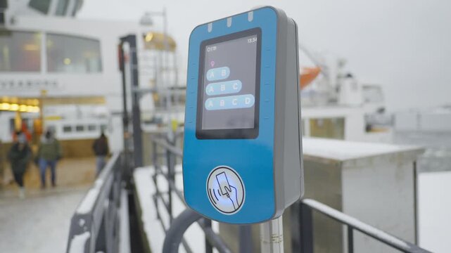 A sleek, modern ticketing kiosk stands at a ferry terminal, showcasing its user-friendly interface. Snow is visible in the background, capturing a chilly winter vibe that contrasts with the bustling a