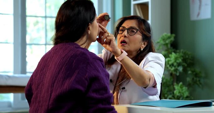 Experienced Indian lady doctor woman checking young female patient in clinic using stethoscope, torch and pulse examination during routine health checkup in modern medical facility