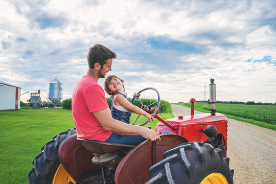 Side view of a smiling man driving a tractor with his son on a farm