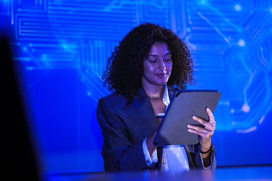 Professional female tech expert interacting with artificial intelligence interface. Woman developer using tablet to analyze digital circuit board data on blue screen. - Powered by Adobe