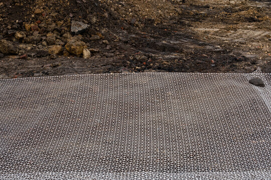 Construction site in process of ground reinforcement with strong plastic geogrid mesh and gravel ready for backfill and compaction