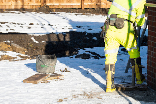 Construction worker scaffolder in bright hi-viz uniform working assembling scaffold platform for bricklayers in winter with snow laying around