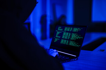 Professional cyber security specialist monitoring network safety. Tech expert in hoodie analyzing code to protect digital system from hacker threats in dark office.