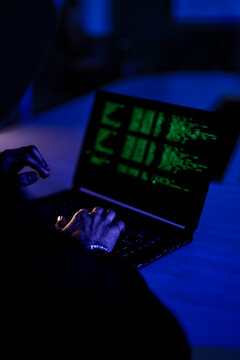 Hardworking software developer writing complex code on laptop at night. Freelance programmer working late on new digital project in modern dark blue workspace.
