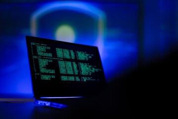 Hardworking software developer writing complex code on laptop at night. Freelance programmer working late on new digital project in modern dark blue workspace