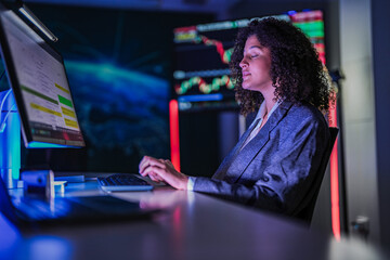 Professional female traders analyzing stock market trends. Business team monitoring financial investment growth graphs on computer screens in modern night office.