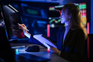 Professional female trader analyzing global stock market trends. Businesswoman typing financial investment data on laptop in modern night office with world map background.
