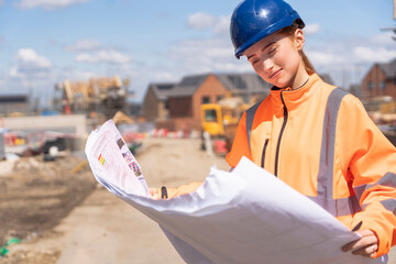Builder woman working on construction site and using blueprints to check works progress © Iryna