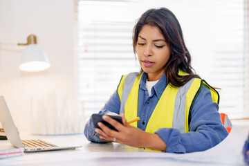 Female land surveyor reviews plans while using smartphone and laptop during office hours at project site