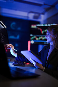 Cyber security specialist analyzing binary code on digital monitor. Female tech expert with tablet checking network safety system in dark control room at night.
