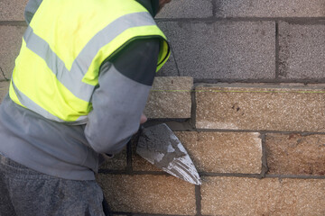Bricklayer constructing stone wall using stone blocks, cement mortar mix and trowel