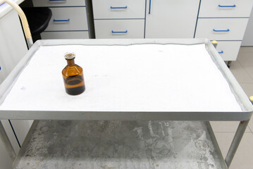 Laboratory transport trolley made of metal, with two shelves. White protective paper on the top shelf, various laboratory items on it.