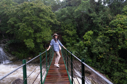 Young woman standing on a suspension bridge above Bambarakiri Ella in Sri Lanka. Female traveler enjoying nature, adventure travel and tropical landscape, freedom and exploration concept.