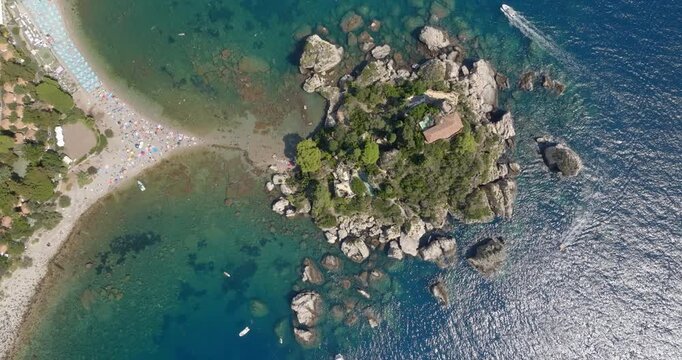 Aerial zenith view of Isola Bella, a small island located near Taormina, in province of Messina, Sicily, Italy. It is a rocky islet surrounded by crystal-clear blue sea. It is a sunny summer morning.