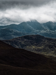 A moody landscape with layers of mountains receding into the distance under a heavy, overcast sky. A serene, yet dramatic scene unfolds.