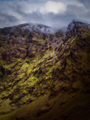 Green mountain rising into a misty sky. The rugged terrain is softened by fog and vegetation, creating a contrast of texture and color.