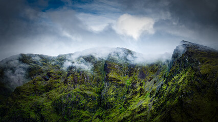 Lush green mountain face disappearing into the low-hanging clouds conveys a sense of mystery and the raw beauty of the wilderness.