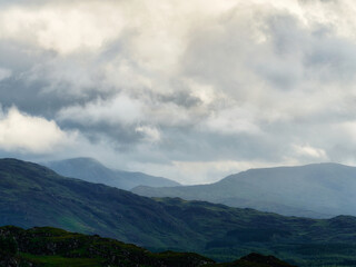 Landscape shows layered mountains under a cloudy sky. The distant peaks fade into the horizon in Killarney National Park, Ireland. The scene is peaceful and majestic.
