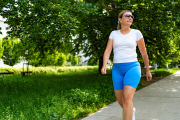 Beautiful middle-aged woman walking in city park on summer day. Front view
