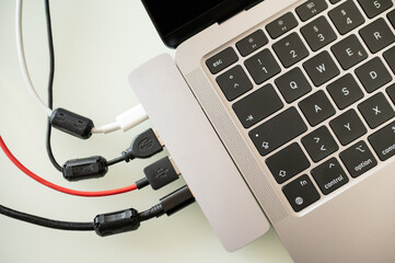 Close-up of a laptop with multiple USB cables and adapters connected through a hub, illustrating modern connectivity, data transfer, charging, and cable management in a workspace setup.