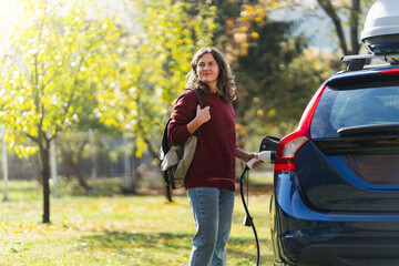 Woman traveler with backpack next to charging electric ca