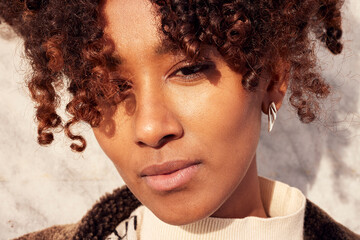 Portrait of a young woman with curly hair in warm sunlight, close up for a natural fashion mood