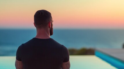 Man looks at sunset over the ocean from a poolside location in evening