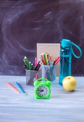 Alarm clock, water, lunchbox, apple and school supplies on table, back to school