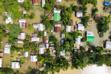 An aerial view shows a flood-affected village with homes and surrounding farmland submerged under muddy water, highlighting the scale of inundation after heavy rainfall