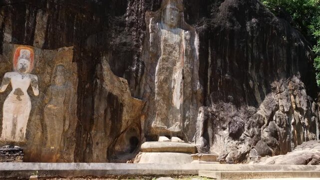 A woman takes off her shoes and walks along an ancient path to a monument in Sri Lanka.Ancient Buduruwagala rock carvings carved into a cliff in Sri Lanka. Large standing Buddha statues surrounded by 
