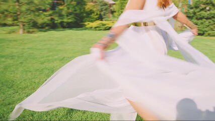 unrecognizable silhouette Happy joyful fantasy woman greek goddess dancing spinning long old style silk white dress flying in wind slow motion. Cheerful fairy girl bride. Day sun light green park