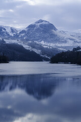 The majestic peak of Txindoki emerges from the winter clouds above the cold waters of the Ibiur reservoir.