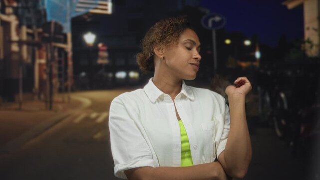 Woman holding feather duster with crossed arms on city street at night, looking sideways with a dismissive glance; indifference.