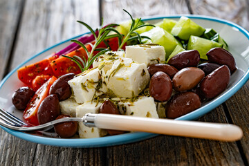 Greek salad - tomatoes with feta cheese, cucumber, red onion and kalamata olives on wooden table