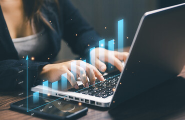 Businesswoman working on laptop with rising bar graph, symbolizing revenue growth, business performance, financial success, data-driven decision making, and corporate strategy.