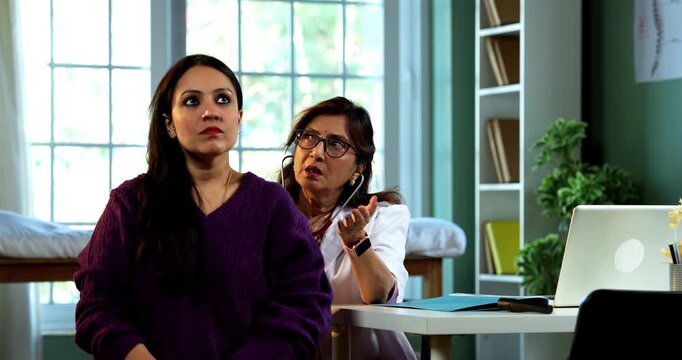 Experienced Indian lady doctor woman checking young female patient in clinic using stethoscope, torch and pulse examination during routine health checkup in modern medical facility