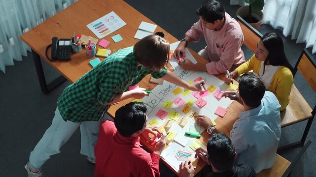 Close up of professional business team hands writing and putting sticky note on scrum task board. Top view of project manager write task and use kanban board to manage time and workflow. Convocation.