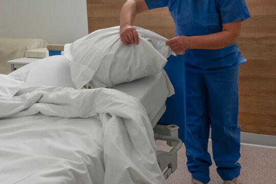 Nurse arranges blankets and pillows on a hospital bed