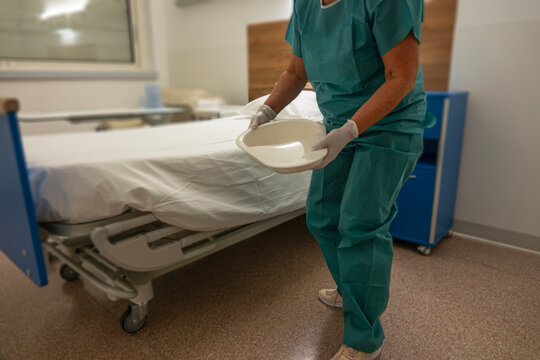 Nurse prepares to assist patient with bedpan in a hospital room setting