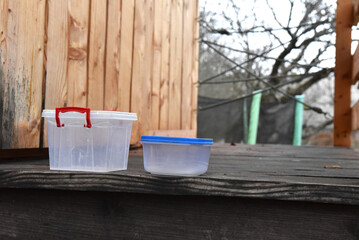 Clear plastic food storage containers with colored lids, one with a red handle, for outdoor use or home organization