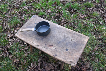 Small black speckled cooking pot with wooden handle on rustic wooden bench outdoors for camping
