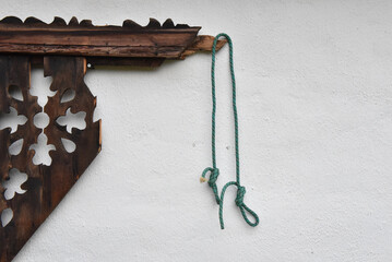 Figure eight on a bight knot, with an overhand safety knot tied in green rope hanging from a carved wooden eave on a white wall