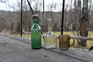Rustic outdoor display of vintage green and clear glass bottles and amber mug on wooden table