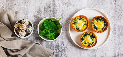 Eggs, spinach and cheese baked in tartlets on a plate on the table top view web banner