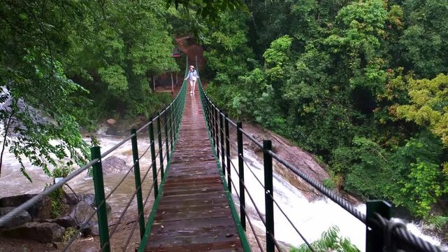 Young woman standing on a suspension bridge above Bambarakiri Ella in Sri Lanka. Female traveler enjoying nature, adventure travel and tropical landscape, freedom and exploration concept.