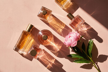 Elegant flat lay of luxury perfume bottles and a pink peony flower in bright, direct sunlight. Concept of fragrance, beauty, and summer self-care.