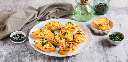 Mini baked sandwiches with crab sticks, egg and cheese on a plate on the table web banner