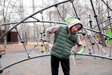 A man in a tracksuit and hat does body bends on an outdoor sports ground. Exercising in cold weather.