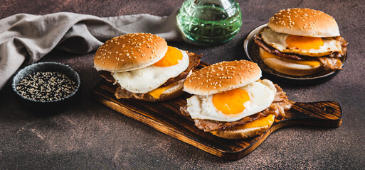 Burgers with fried egg, bacon and cheese on a board on a table web banner