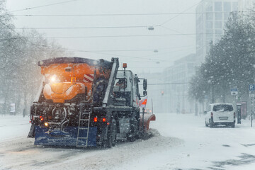 Snowplow truck removing dirty snow from city street on highway during heavy snowfalls. Traffic road situation. Bad weather conditions forecast for drivers. Seasonal road maintenance Europe Germany